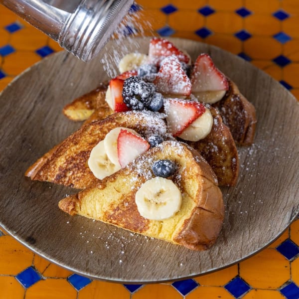 Powdered sugar being sprinkled over Lazy Daisy's French toast with berries and bananas.