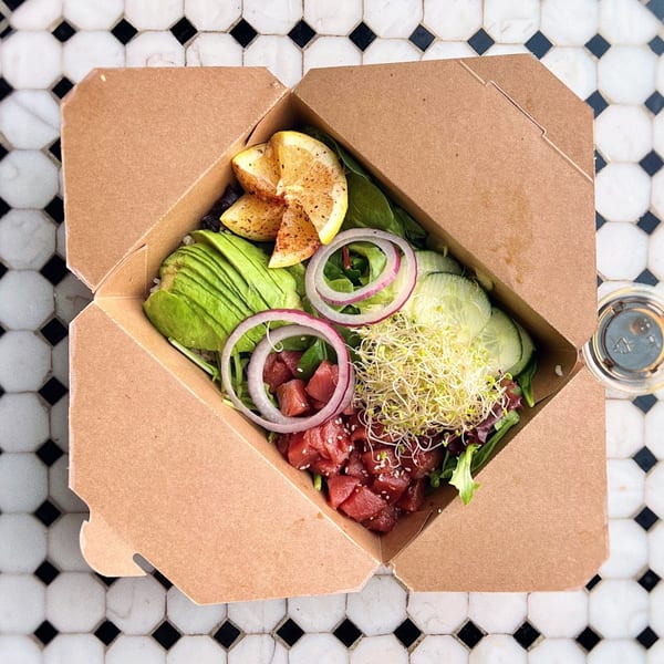 Lazy Daisy poke bowl with tuna, avocado, red onion, sprouts, and lemon in a takeout box.