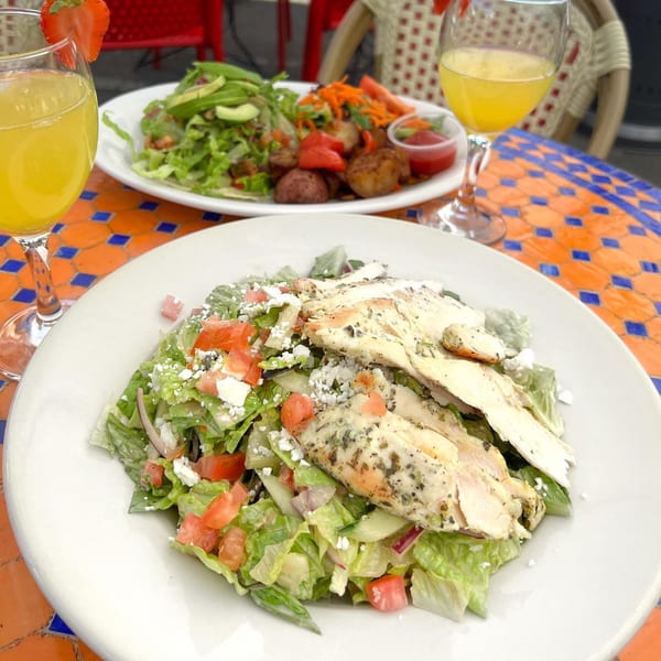 Lazy Daisy chicken salad with tomatoes and feta, another salad, and mimosas on a mosaic table.