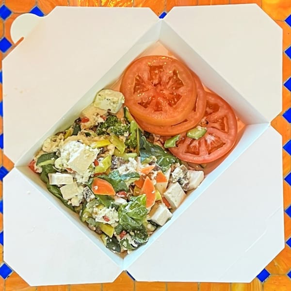 Lazy Daisy's breakfast scramble with vegetables, feta, and sliced tomatoes in a takeout container.