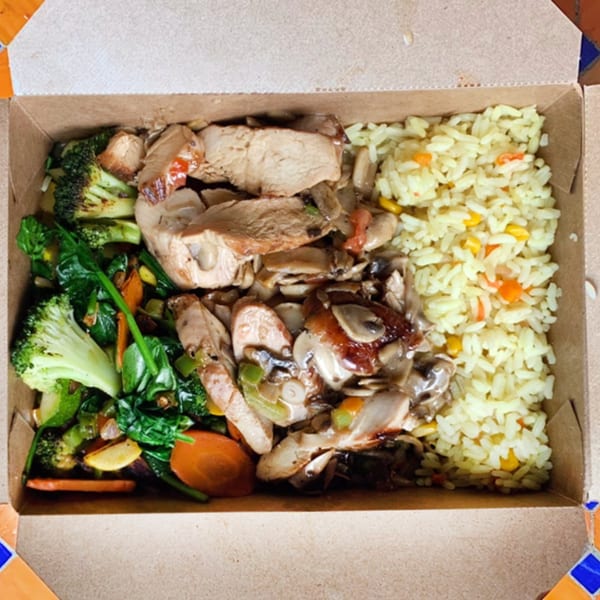 A takeout box filled with sliced chicken, mushrooms, mixed vegetables, and yellow rice.