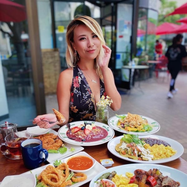 Woman at Lazy Daisy enjoying a large breakfast spread with acai bowl, fried chicken, and onion rings.